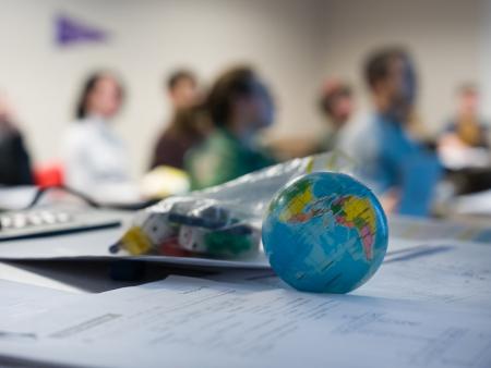 A tennis-ball-sized world globe sits on a desk with a class in the background.