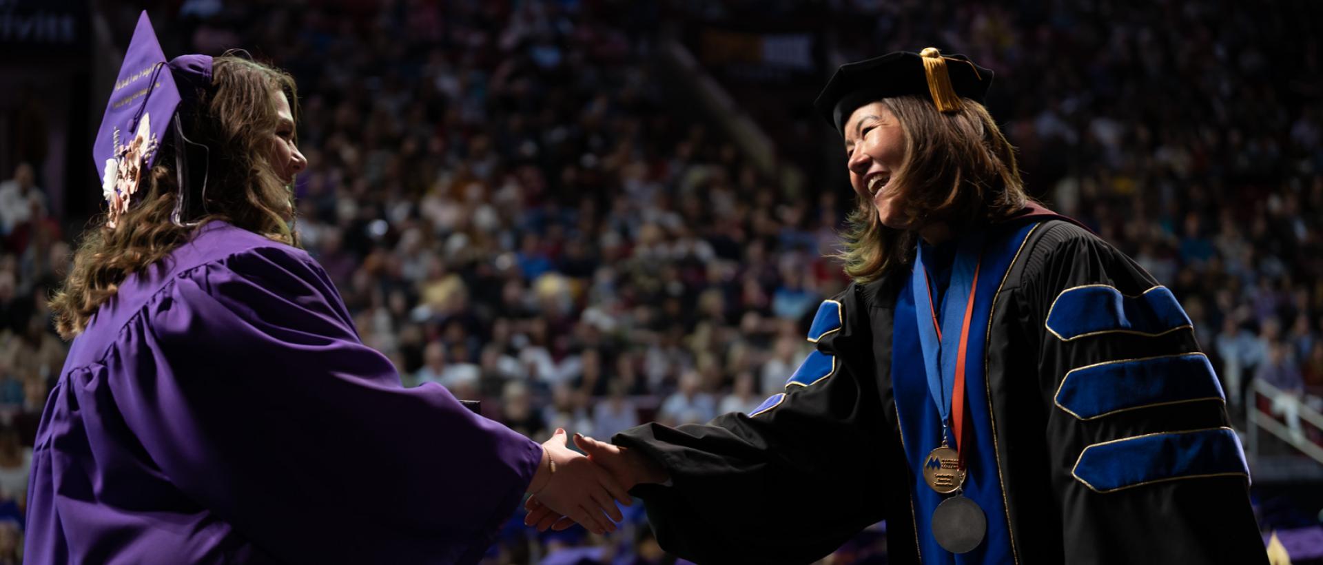 ACC graduate shaking President Stephanie J. Fujii, PhD's hand at Commencement ceremony at Magness Arena.