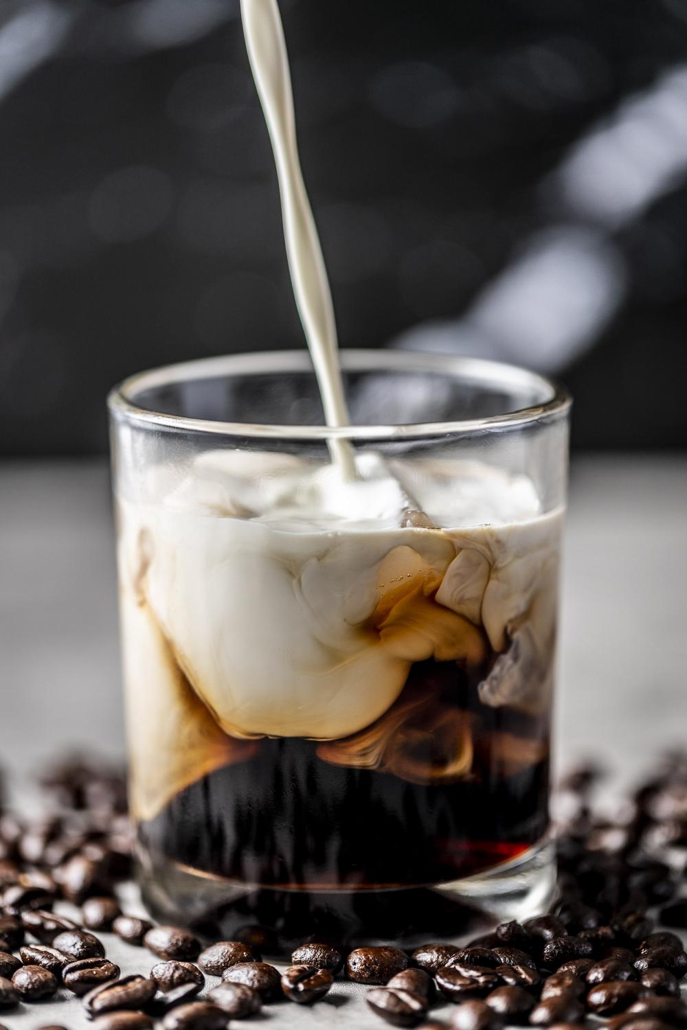 Photo of coffee in clear glass with cream being poured into it - photo by Mercedes Gania