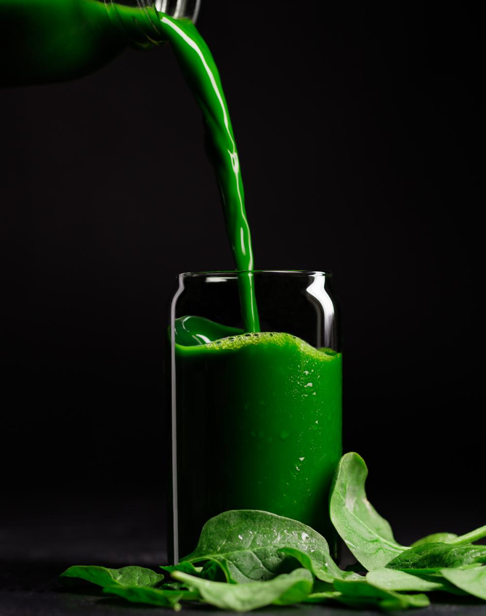 Photo of green juice being poured into a glass with spinach in front by Kate Blakeman