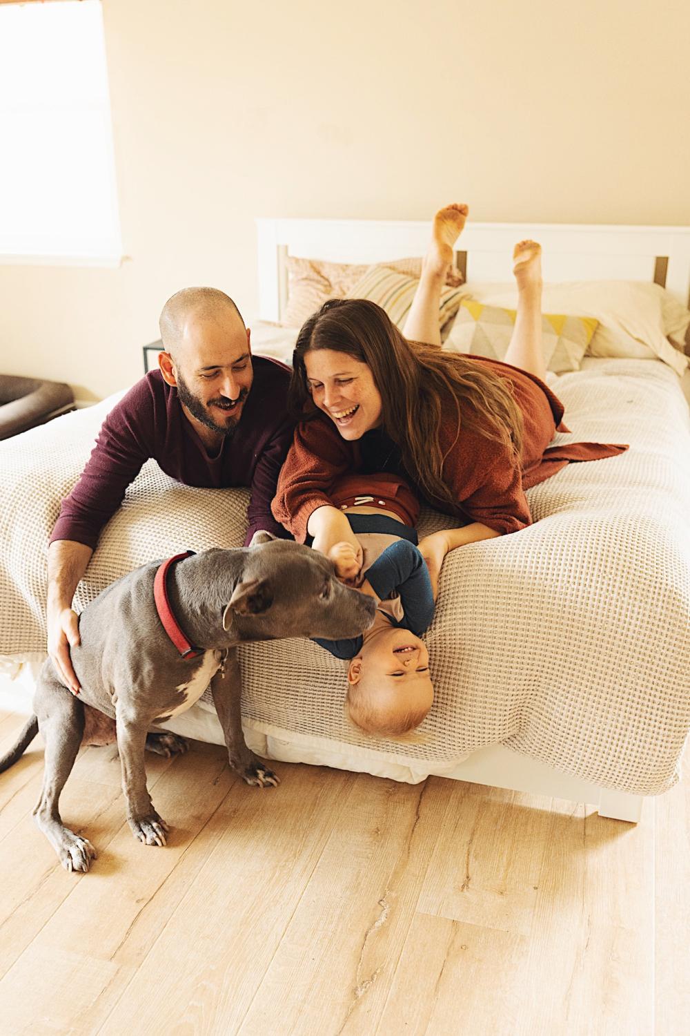 Family portrait of family smiling and laughing while sitting on a bed.