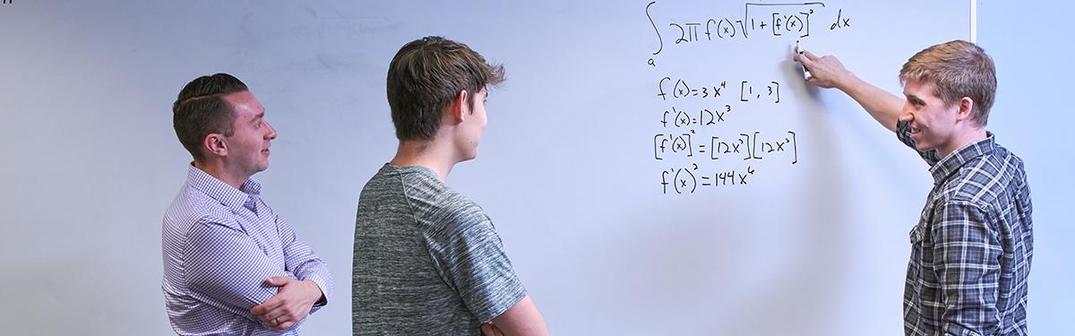 Students at a white board working on a math problem in Academic Support in the ACC Library.