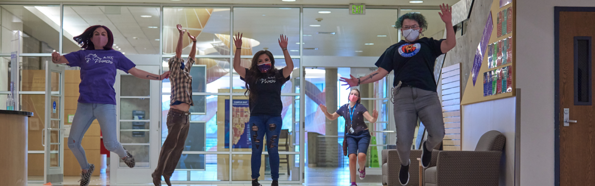 ACC students jumping in the air next to the Welcome Center at the Littleton Campus.