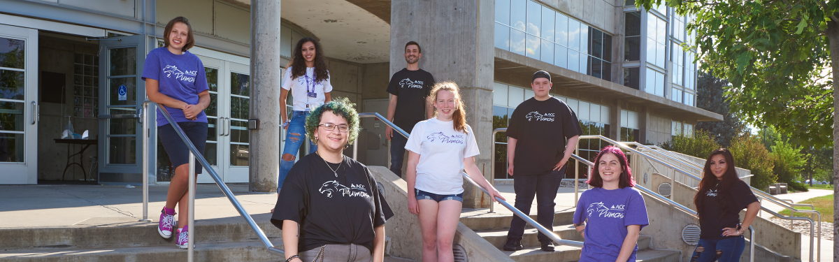 ACC students wearing ACC t-shirts standing on the steps to the main building at the Littleton Campus.