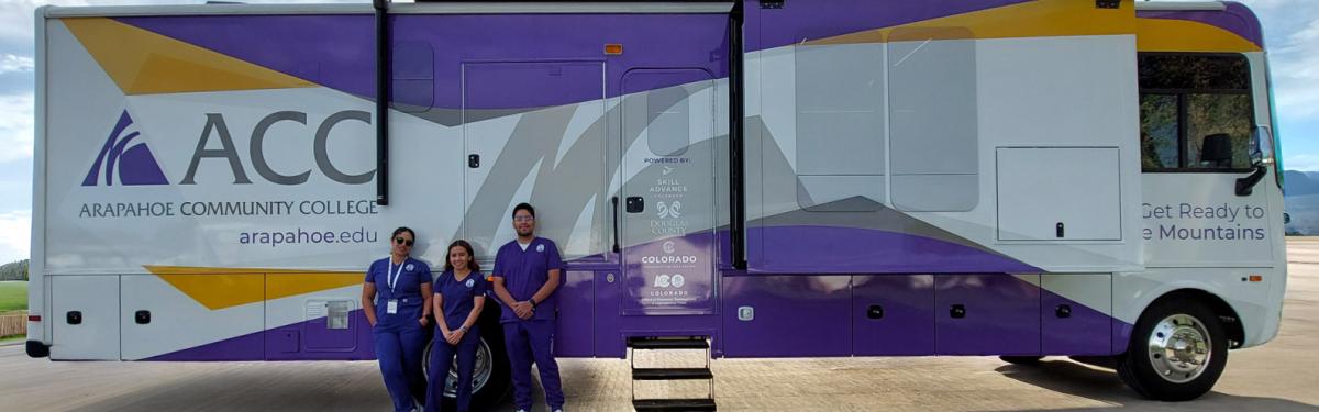 ACC's Mobile Learning Lab with 3 EMT students standing beside it in the Littleton Campus parking lot.