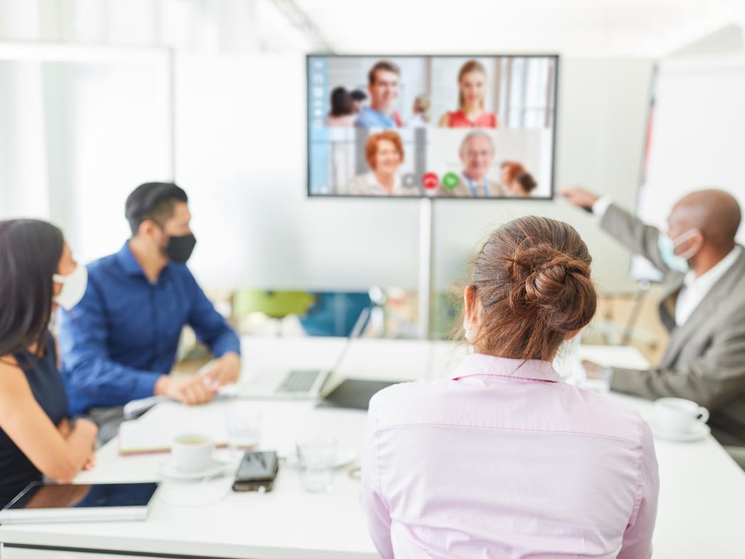 People working in an office, in a meeting with people on video as well.