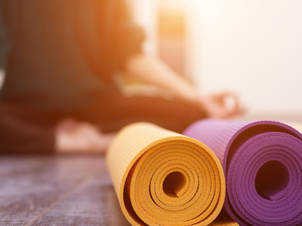 Yoga mats rolled up with yoga student meditating behind them.