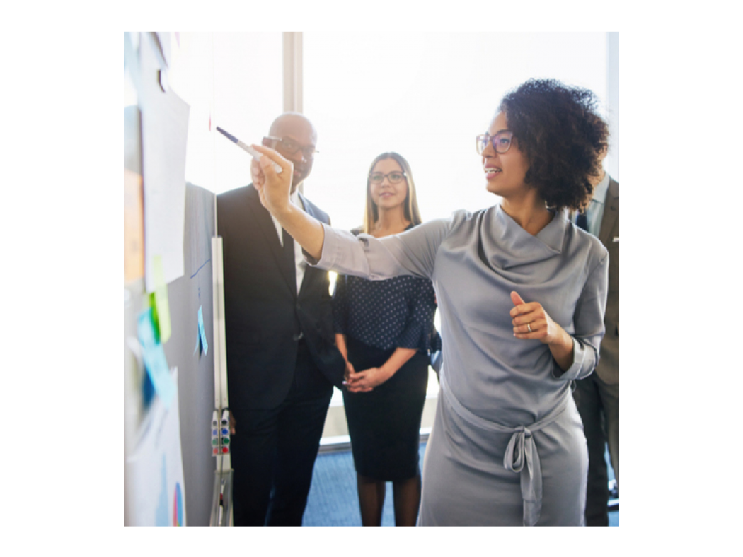 Woman presenting to others while writing on a white board.