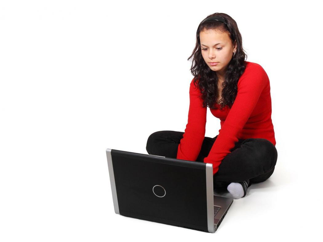 Teen girl sitting on the floor working on a laptop.