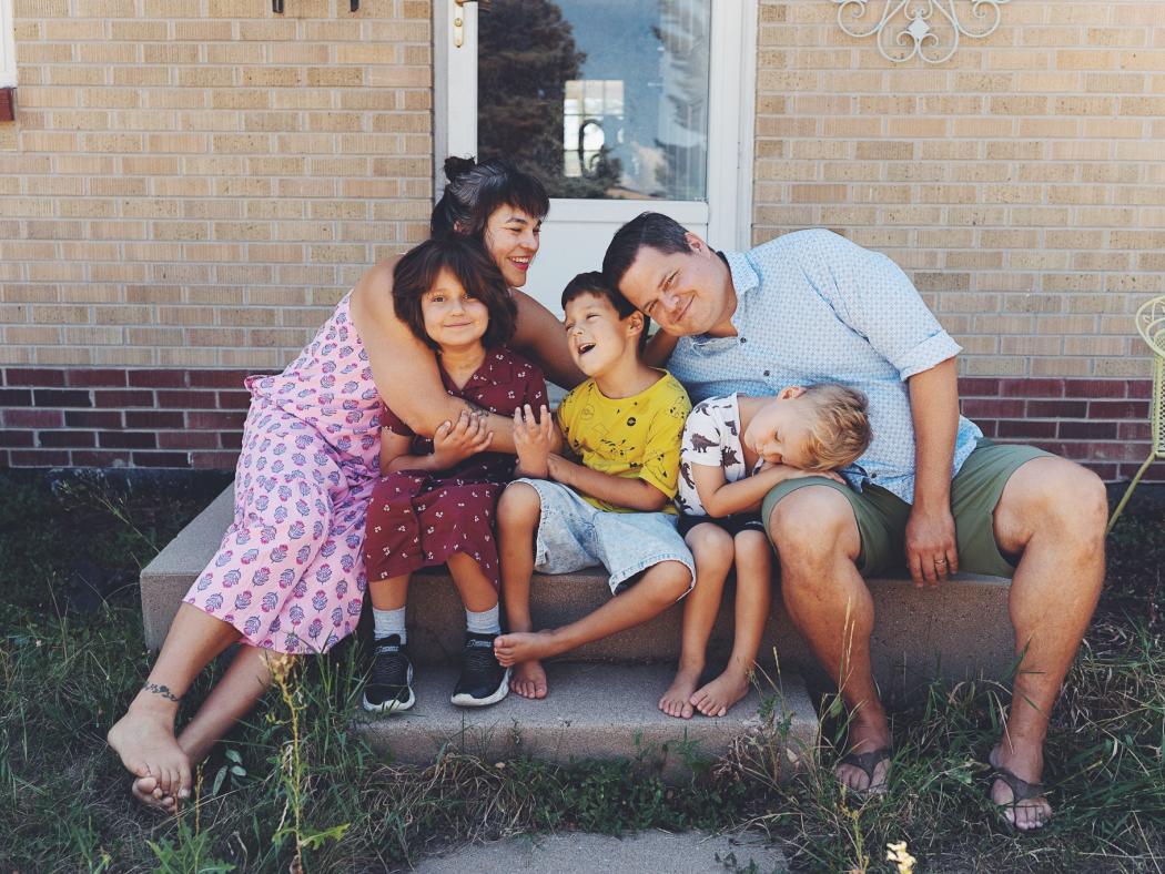 Family hugging and sitting on front step of home.