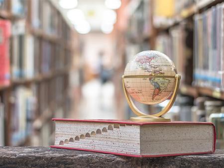 small globe on top of a dictionary in a library.