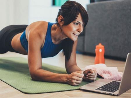 Woman doing a plank while using ACC Sweat On Demand workout videos on laptop.