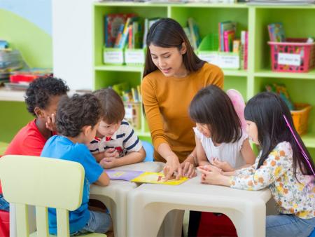 Latina early childhood eduction teacher surrounded by children at a table.