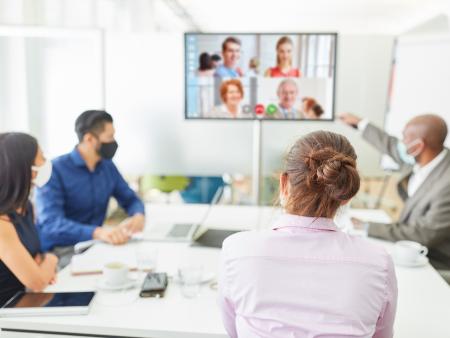 People working in an office, in a meeting with people on video as well.