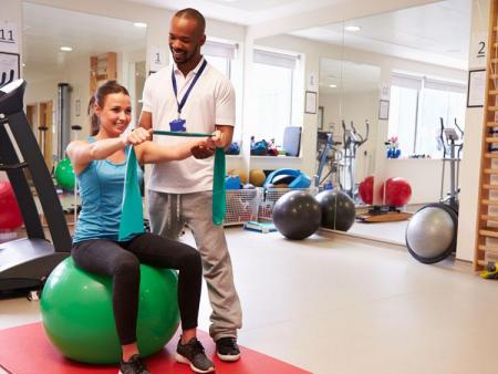 Physical therapist assistant helping women on exercise ball with physical therapy exercises.