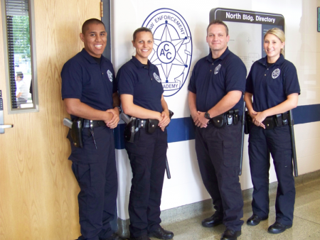 Four ACC Law Enforcement Academy students standing beside an ACC LEA classroom in the North Building at the Littleton Campus.