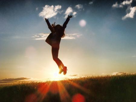 Person jumping in the air backlit by a sunset on the horizon.