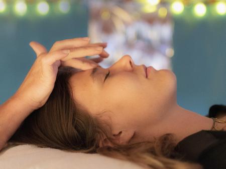 Hands on head of person lying down performing healing Reiki.