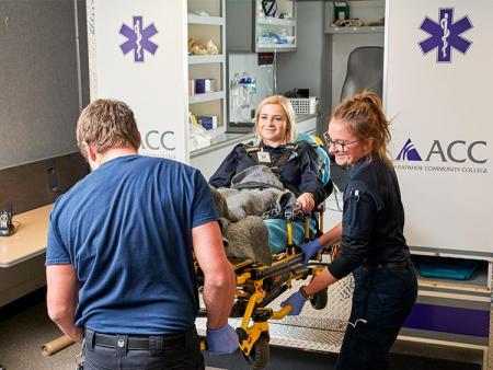 ACC EMT students carrying another student on a gurney out of ACC's mock ambulance.