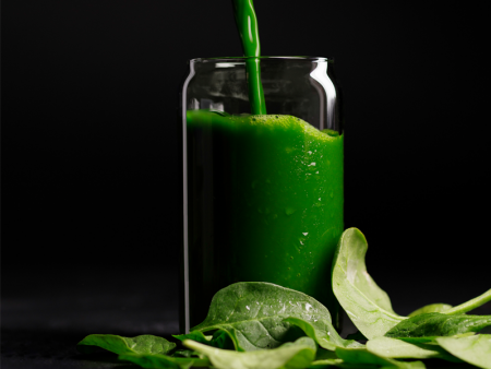 Green juice being poured from container into glass surrounded by leaves - photo by Kate Blakeman