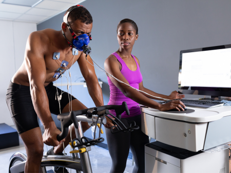 Man riding bike hooked up to medical equipment for testing while woman monitors at a computer next to him.