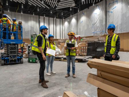 ACC construction management / architecture students wearing safety gear consulting in a warehouse.