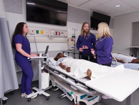ACC Nursing students and instructor around a manikin on a hospital gurney in ACC's Health Innovation Center at the Littleton Campus.