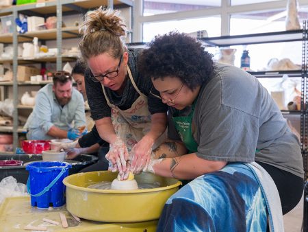 ACC Art faculty member assisting a student with clay at the potter's wheel at the Art & Design Center at the Littleton Campus.
