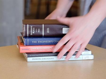 Hands holding 4 engineering text books on top of a desk.