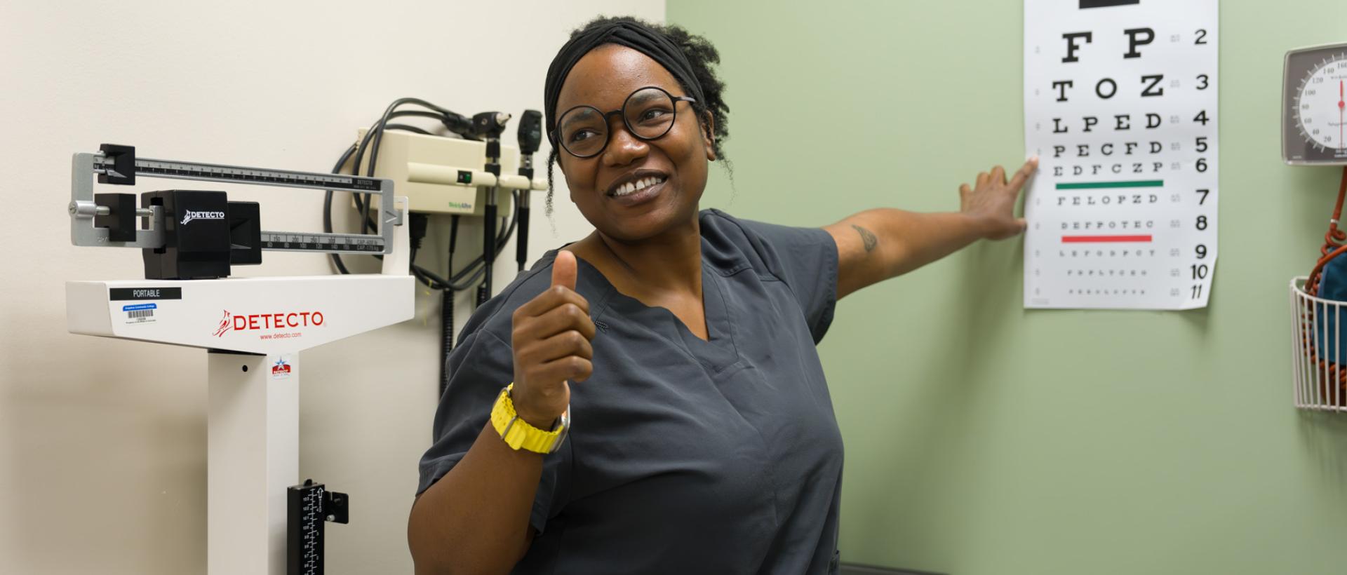 ACC Medical Assistant student in front of eye test giving a thumbs up.