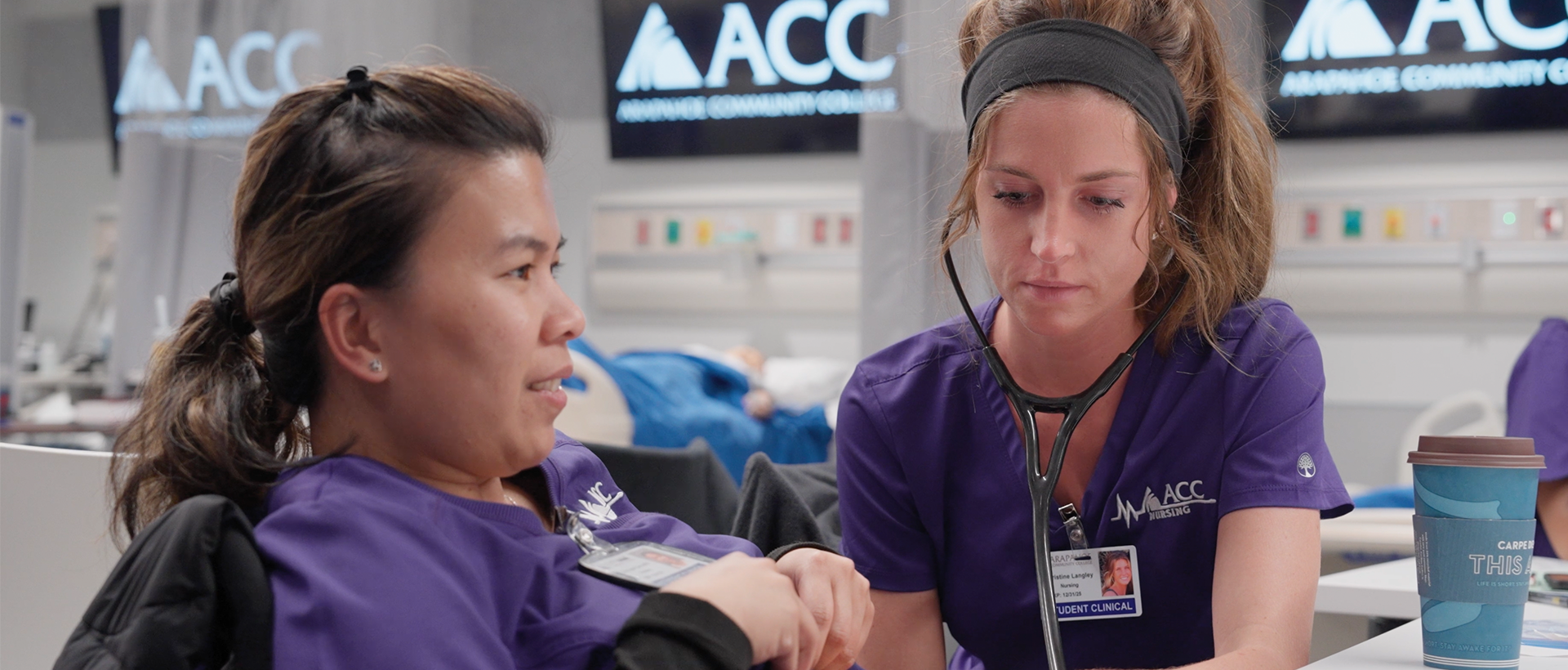 ACC nursing student using a stethoscope to listen to another student's abdomen in the Health Innovation Center at the Littleton Campus.