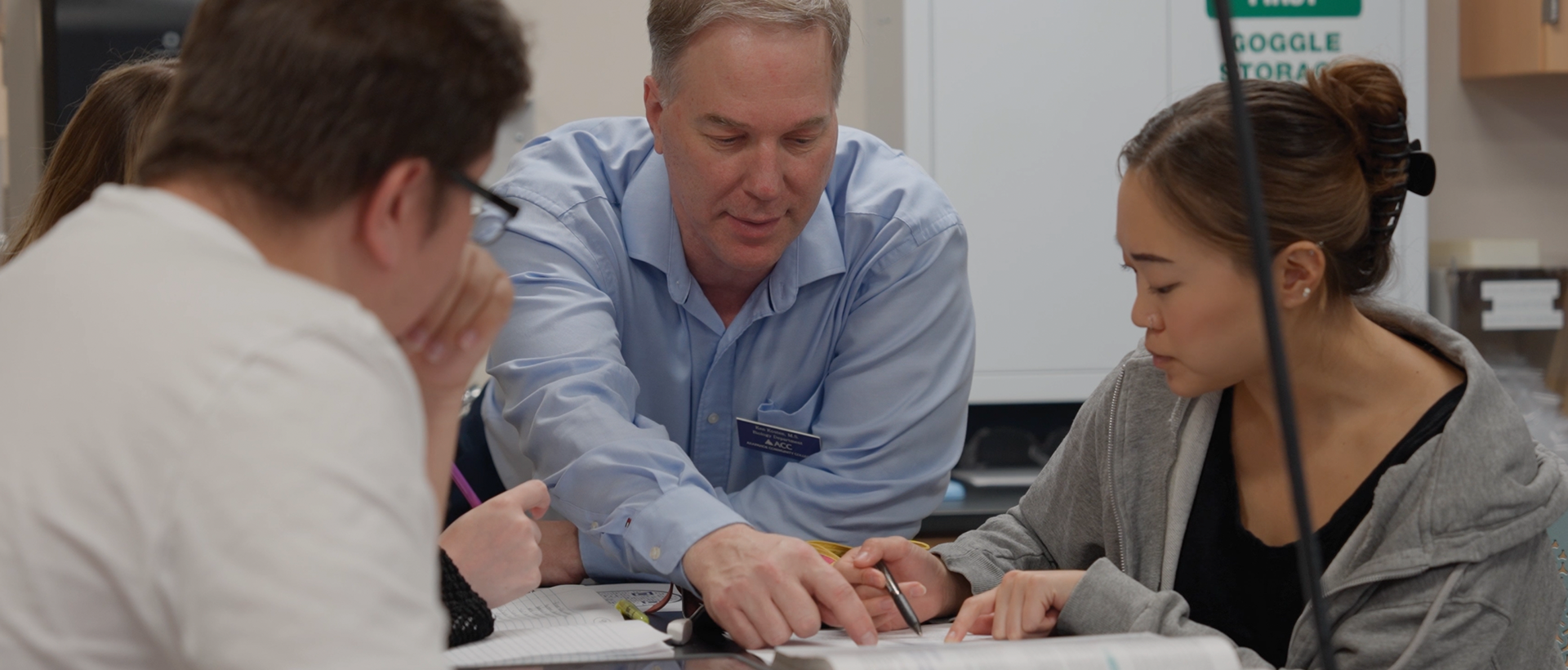 ACC faculty member pointing at a textbook with students looking over at the Littleton Campus.