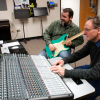 ACC faculty and students in the Music Audio Technology lab playing guitar and working a sound board.