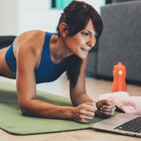 Woman doing a plank while using ACC's Studio SWEAT onDemand on laptop.
