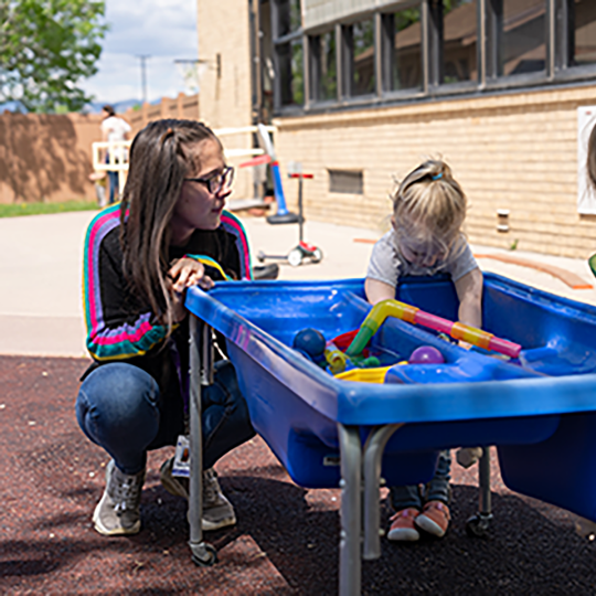 Child playing under supervision of teach at the ACC Child Development Center on the playground.