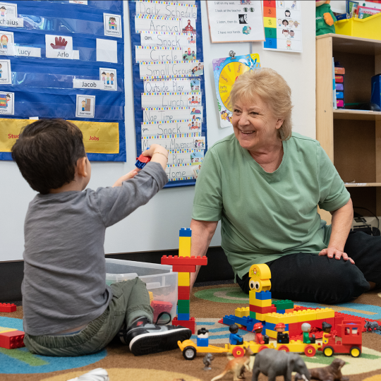 ACC Early Childhood Educator in a child development center classroom with a student playing with stacking blocks.
