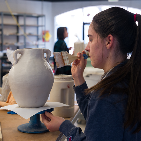 ACC art student applying a glaze to a ceramics piece at the Art & Design Center