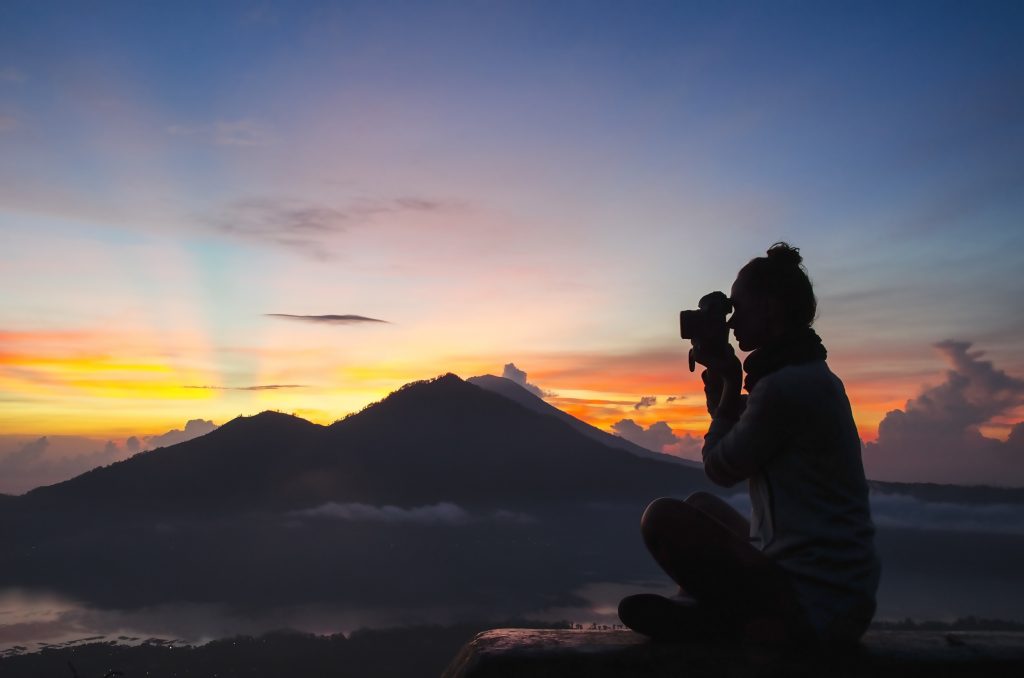 Female photographer taking a picture of sun setting on mountains